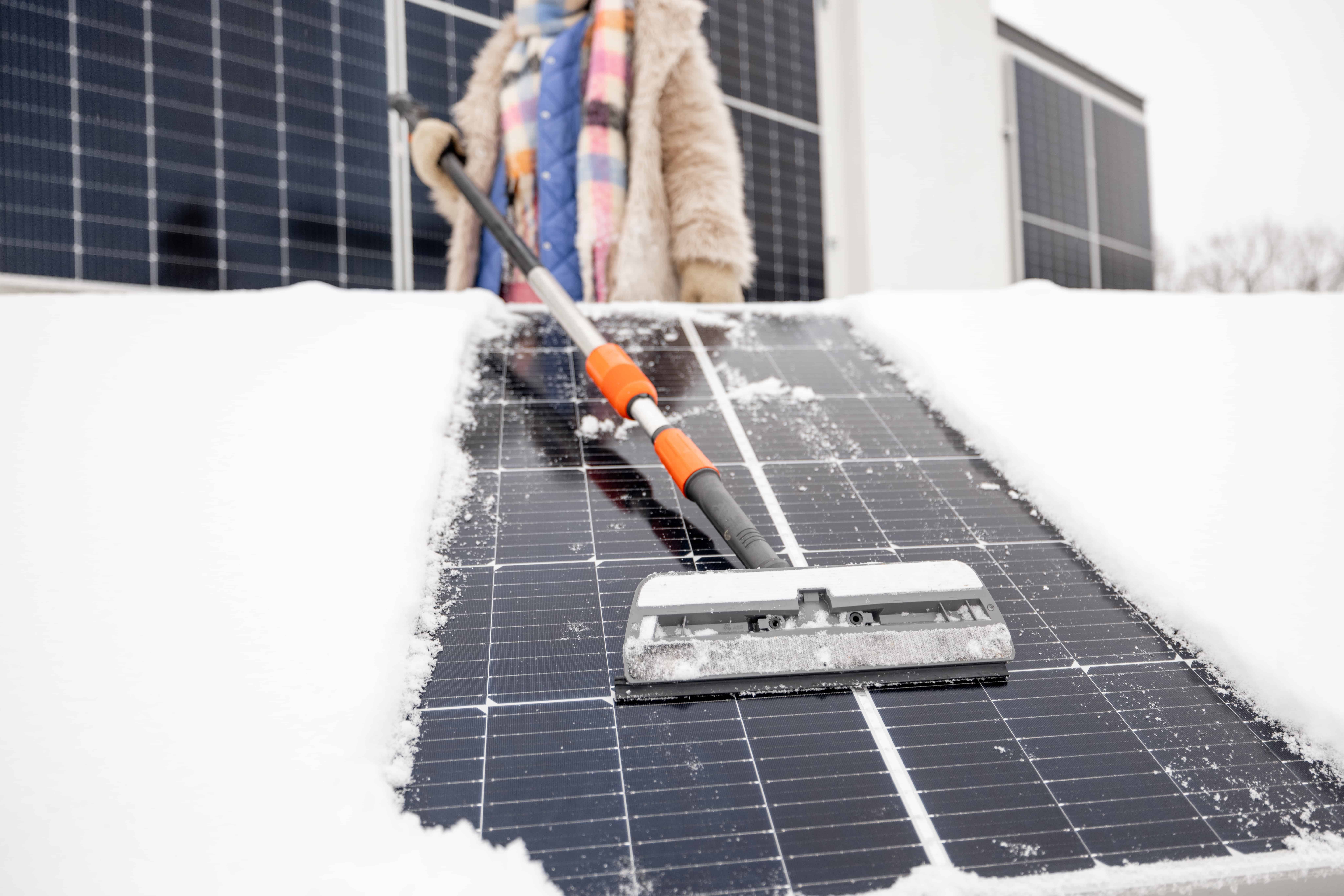 A homeowner cleaning their solar panels off in winter.